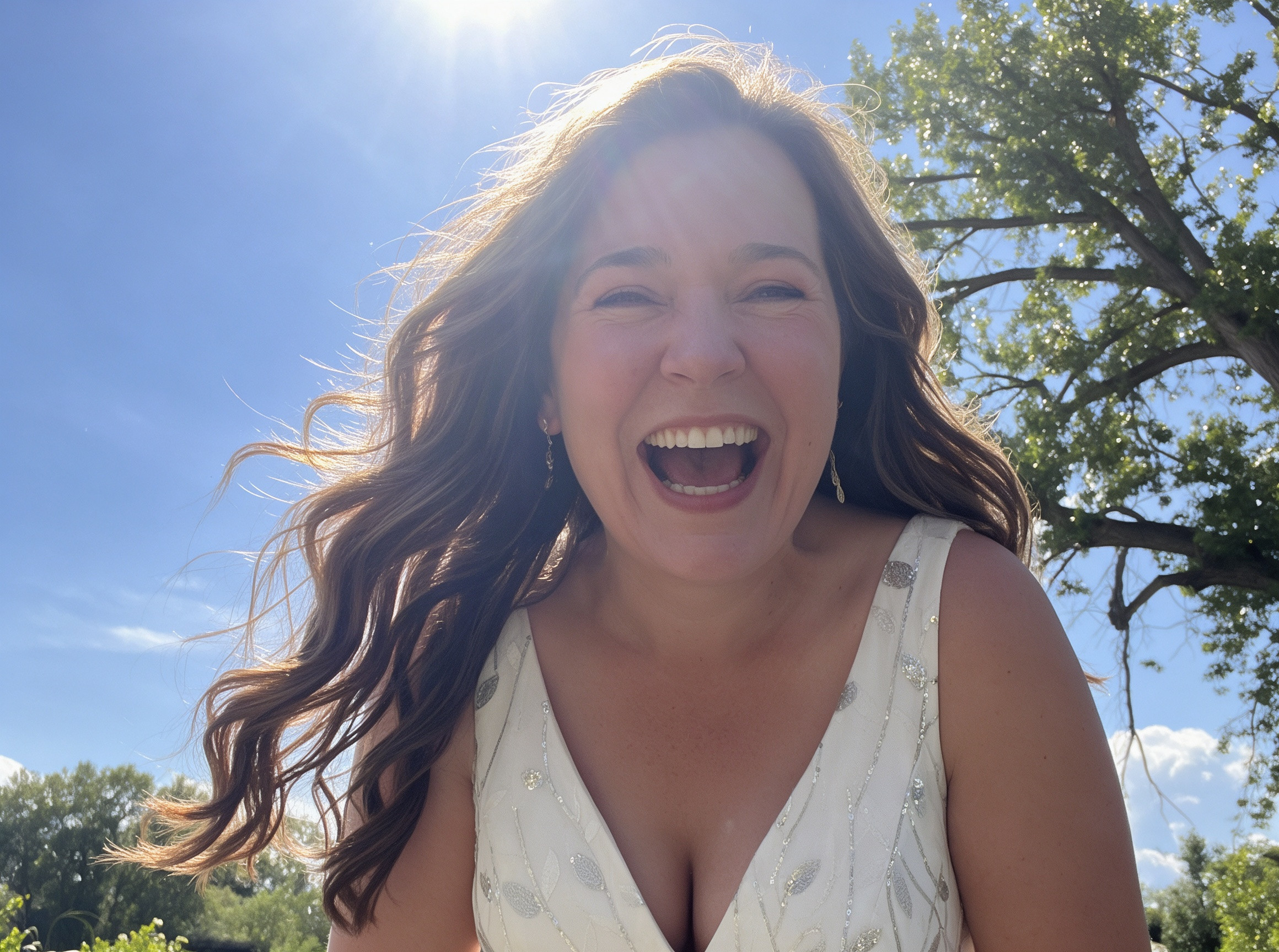 Candid shot of the bride laughing in summer backlight wearing a silver beaded wedding gown