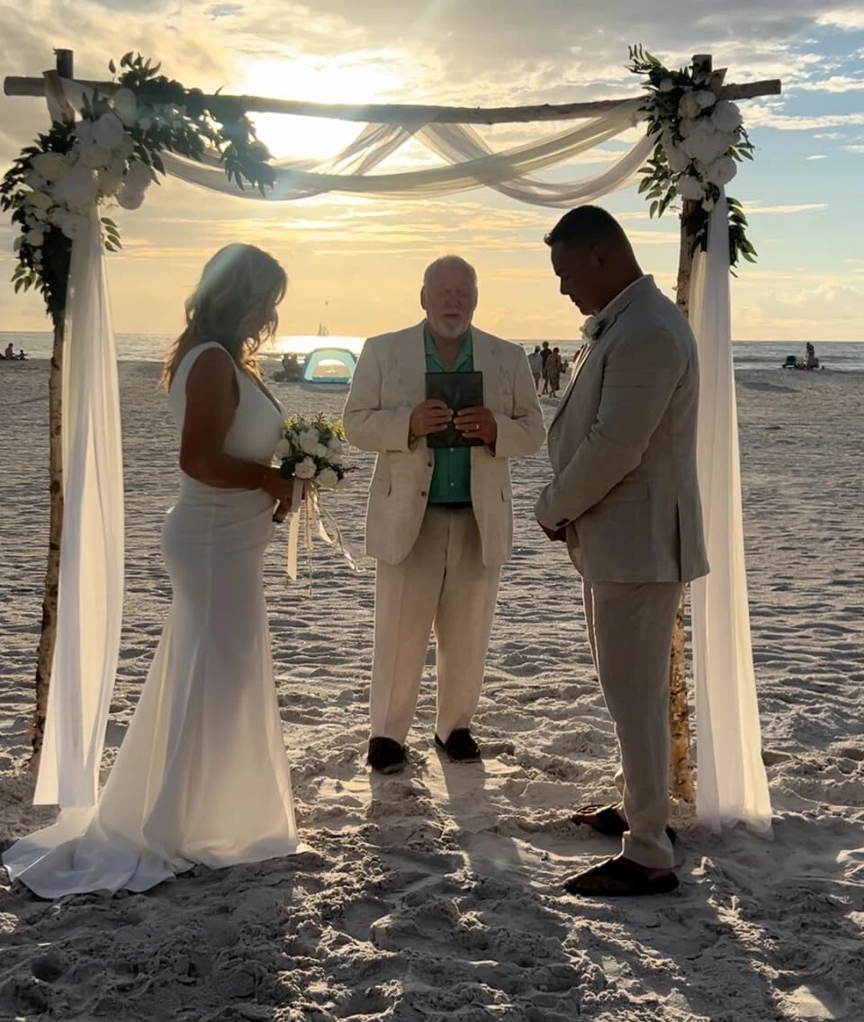 Bride and groom standing beneath a driftwood arch during a sunset beach wedding