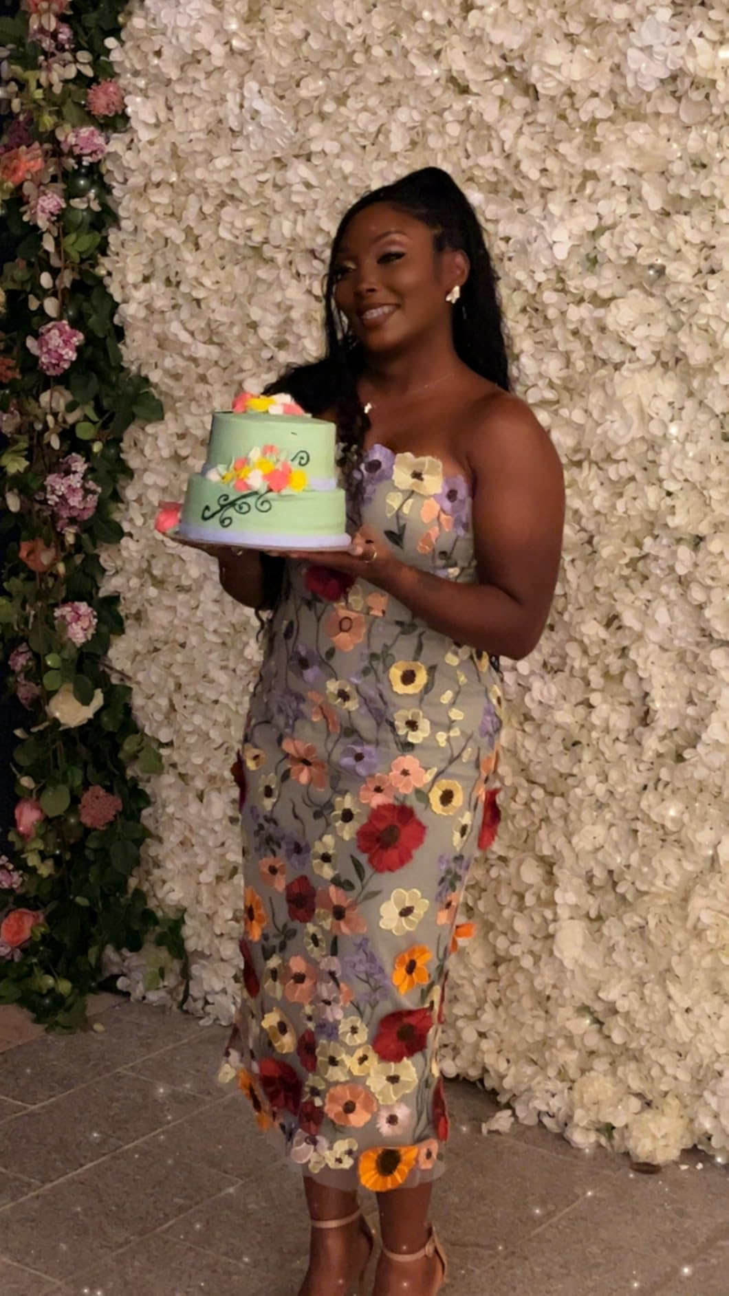 Elegant woman wearing a strapless floral midi dress with a birthday cake
