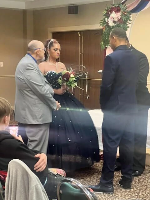 Bride and groom exchanging vows beneath a burgundy and navy wedding arch