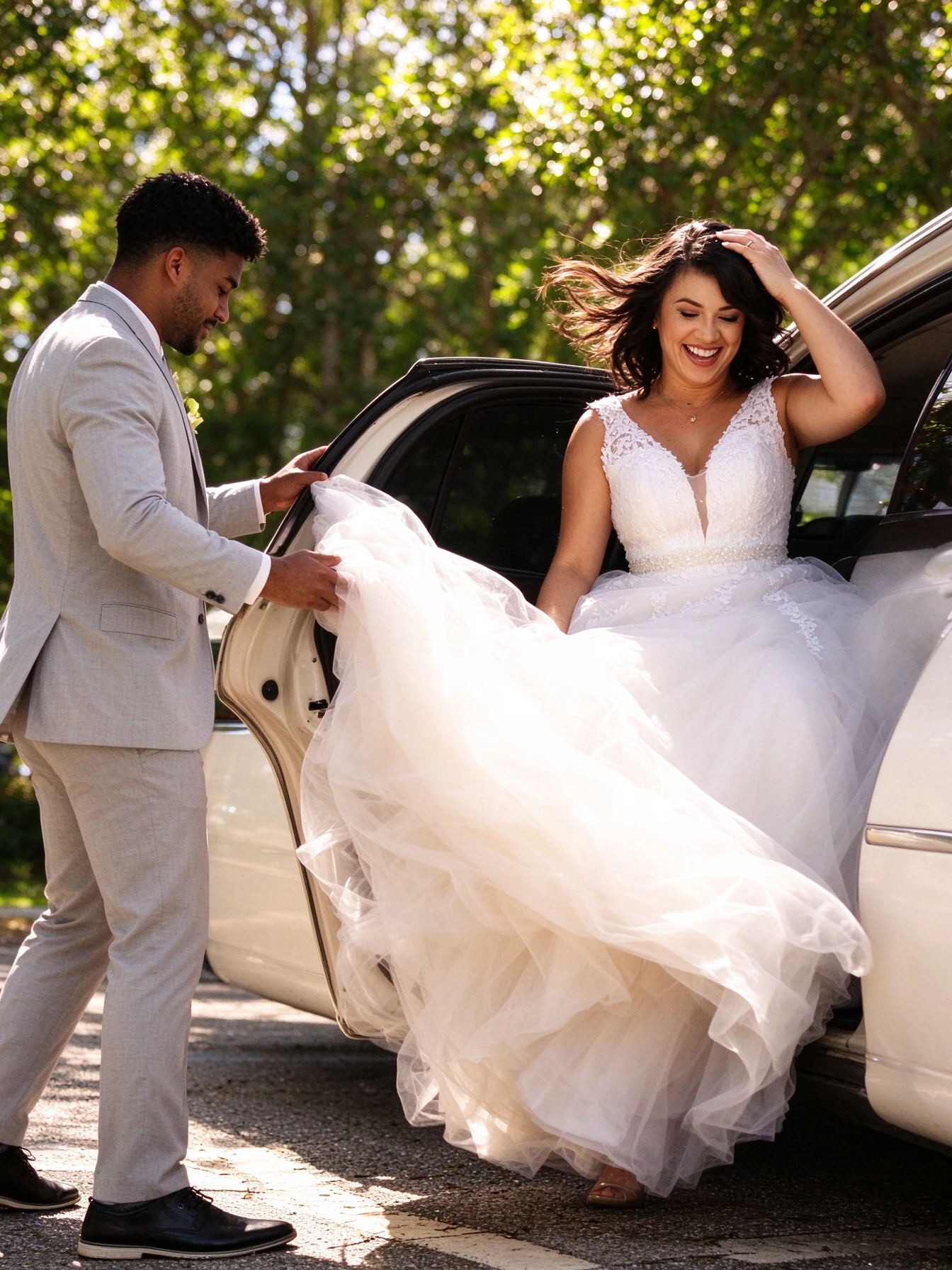 Groom lifting the bride's airy tulle skirt as she steps from the car