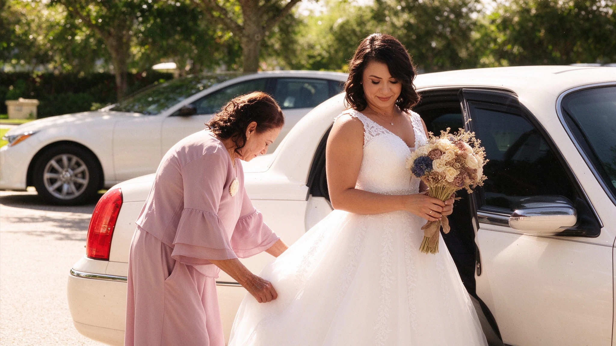 Mother adjusting the bride's tulle skirt beside a white car