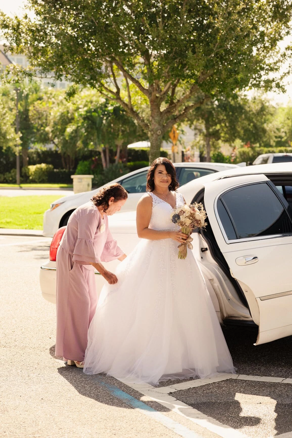 Mother helping the bride adjust her wedding gown beside the car