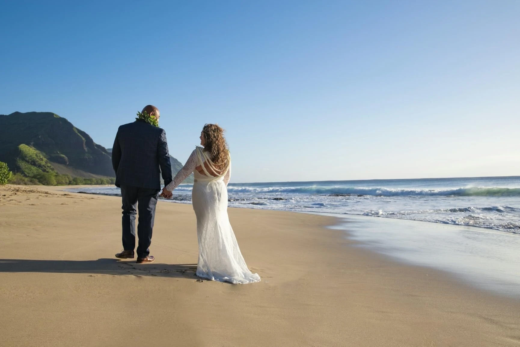 Newlywed couple walking together along the Oahu coast after a beach elopement