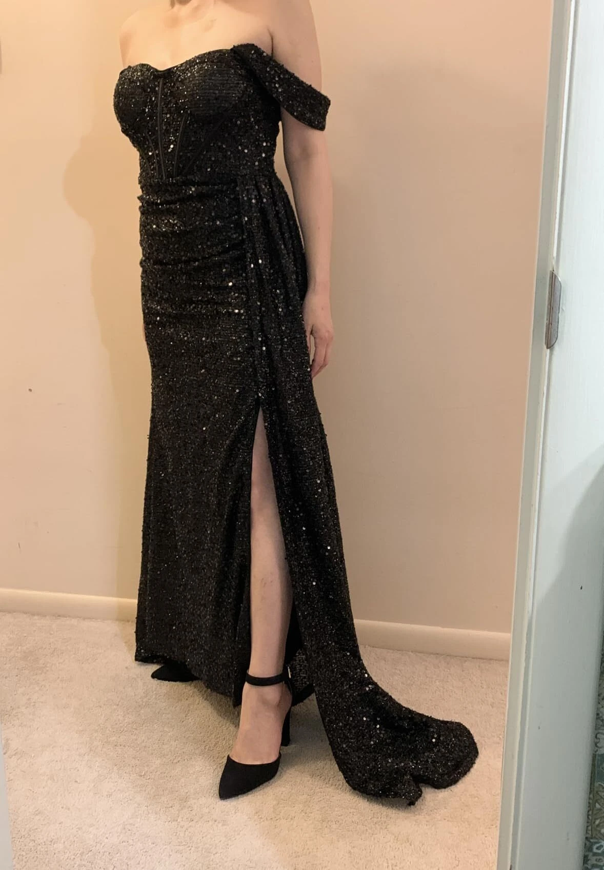 Full-length view of an off-the-shoulder black sequin mermaid prom gown with a slit