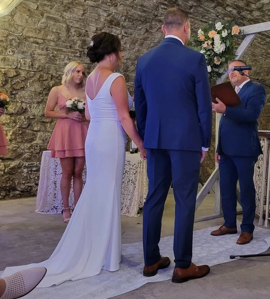 Wedding ceremony seen from behind with bride wearing a white V back crepe gown