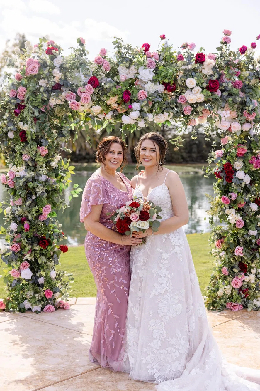 Mother and daughter posing together beneath a floral wedding arch