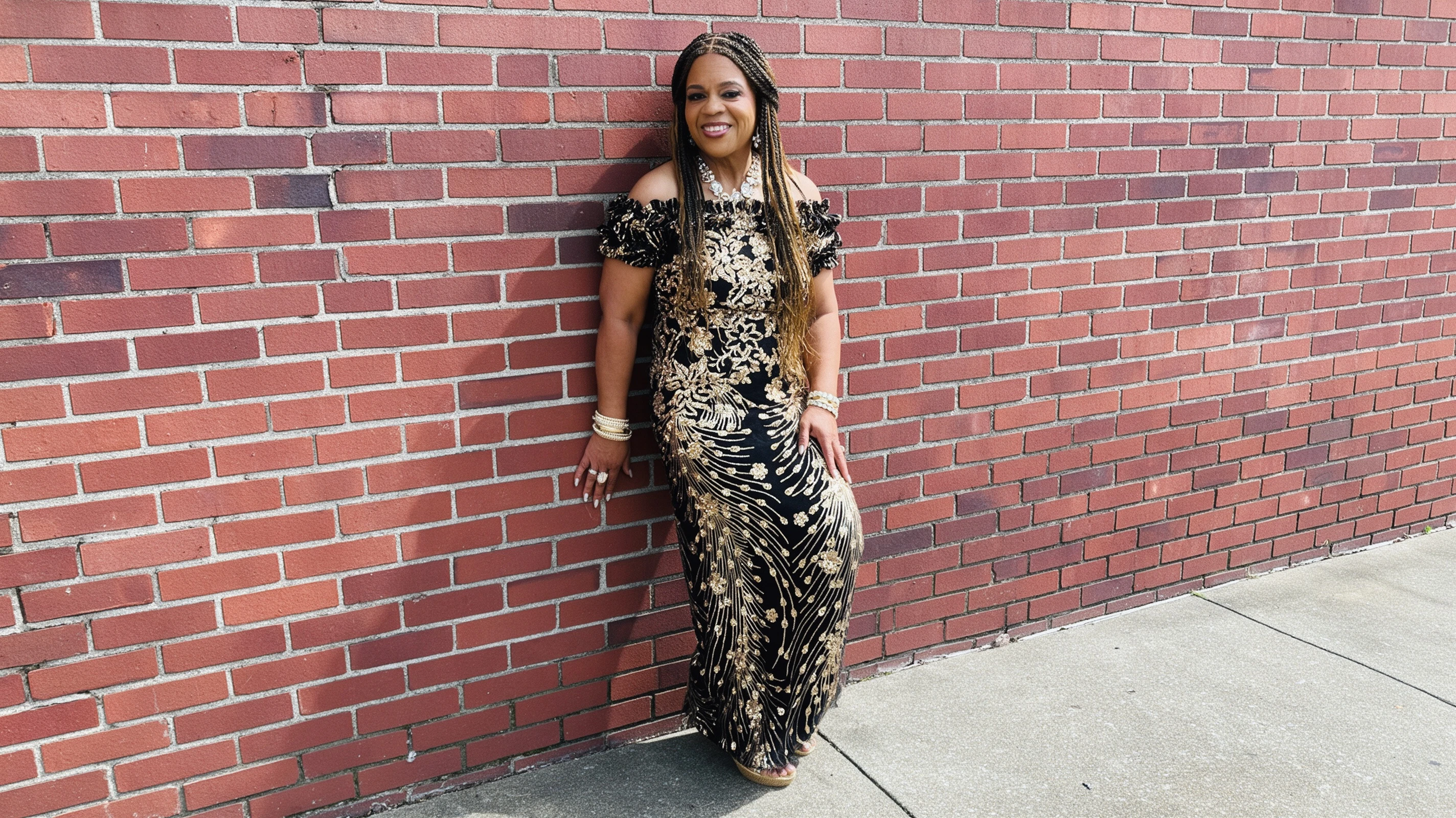 Black and gold sequin evening gown portrait against brick wall