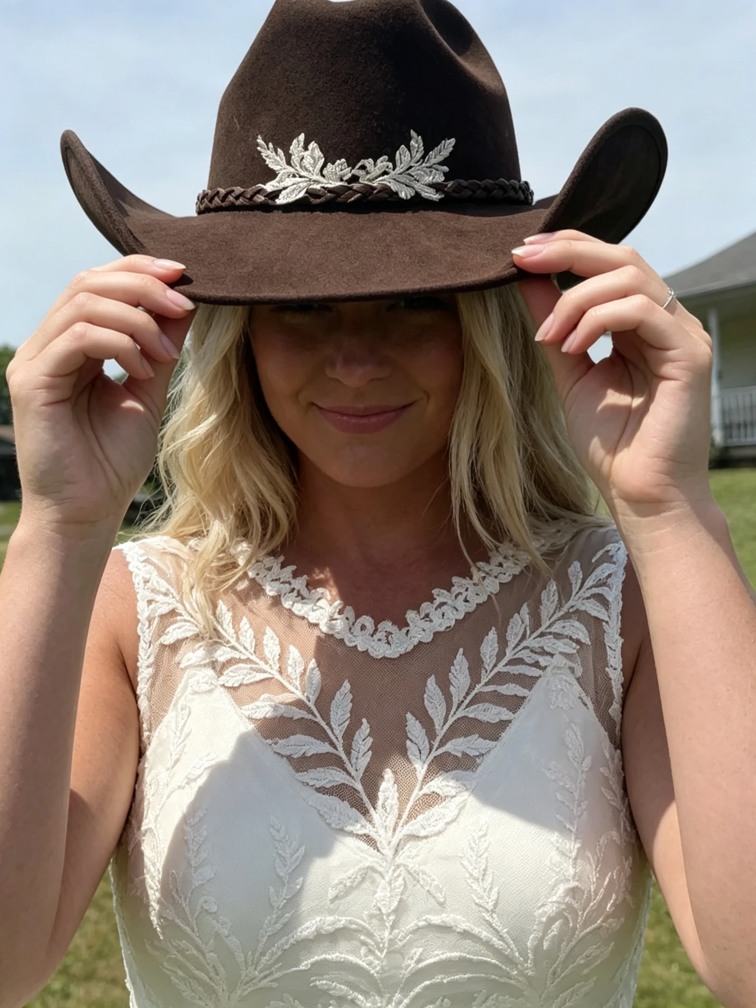 Close up of a sleeveless lace wedding dress styled with a brown western hat