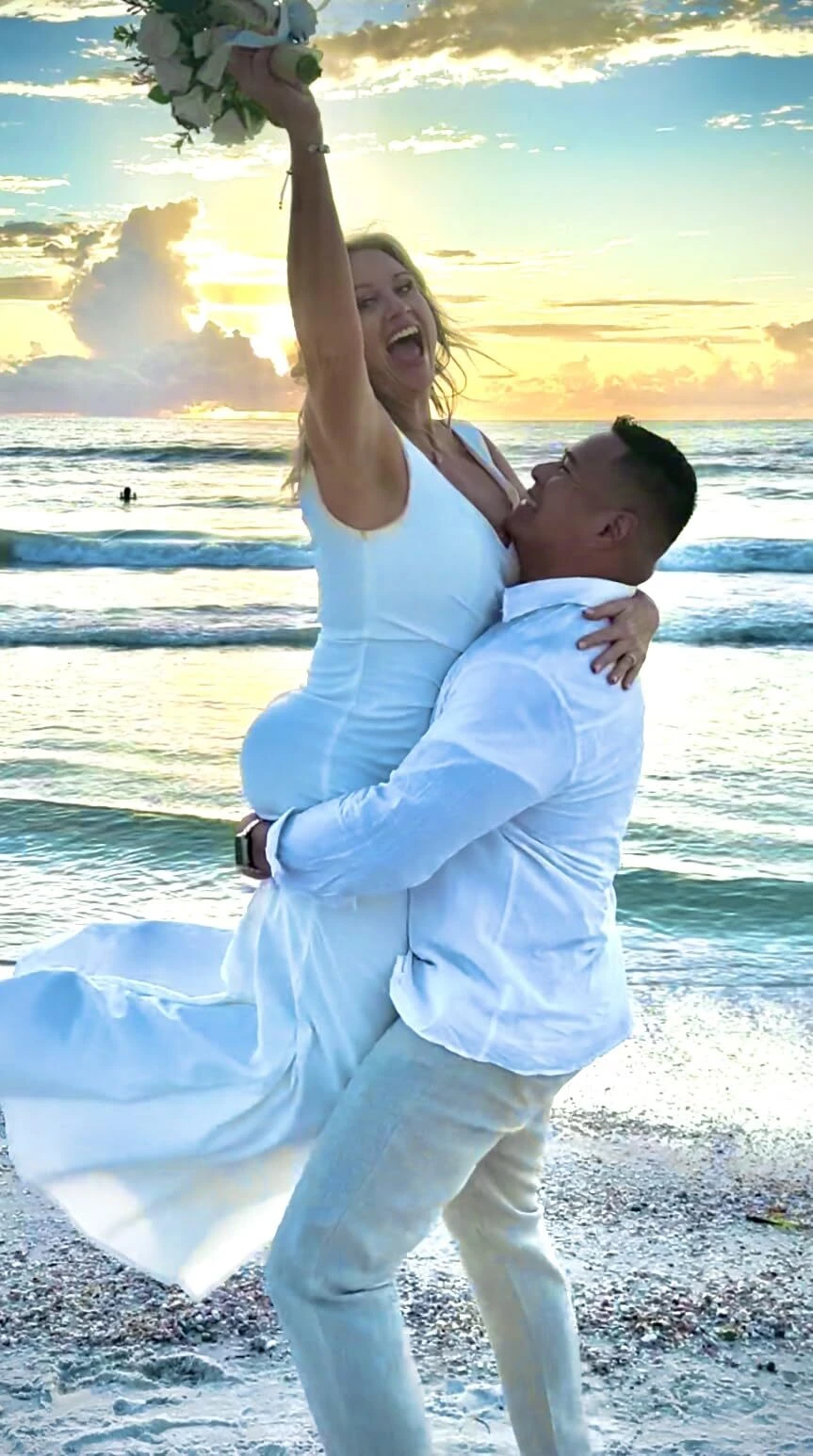 Bride lifted by groom during a sunset beach wedding in a white fit and flare mermaid dress