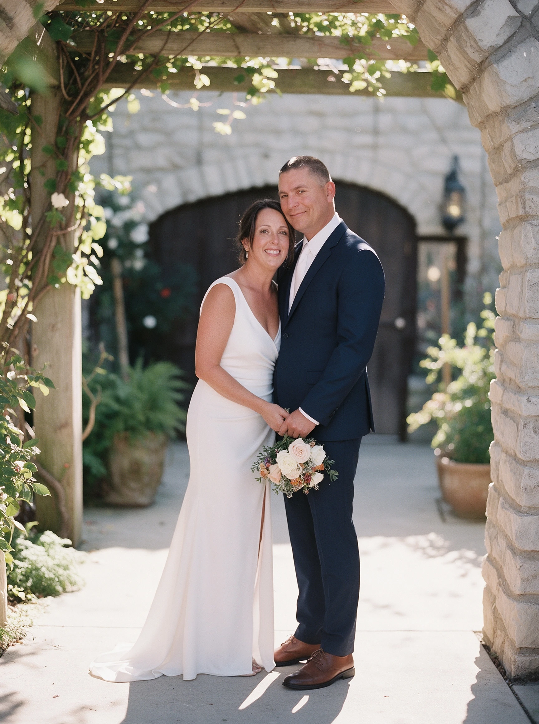 Bride beneath a stone archway wearing her customized white crepe wedding gown