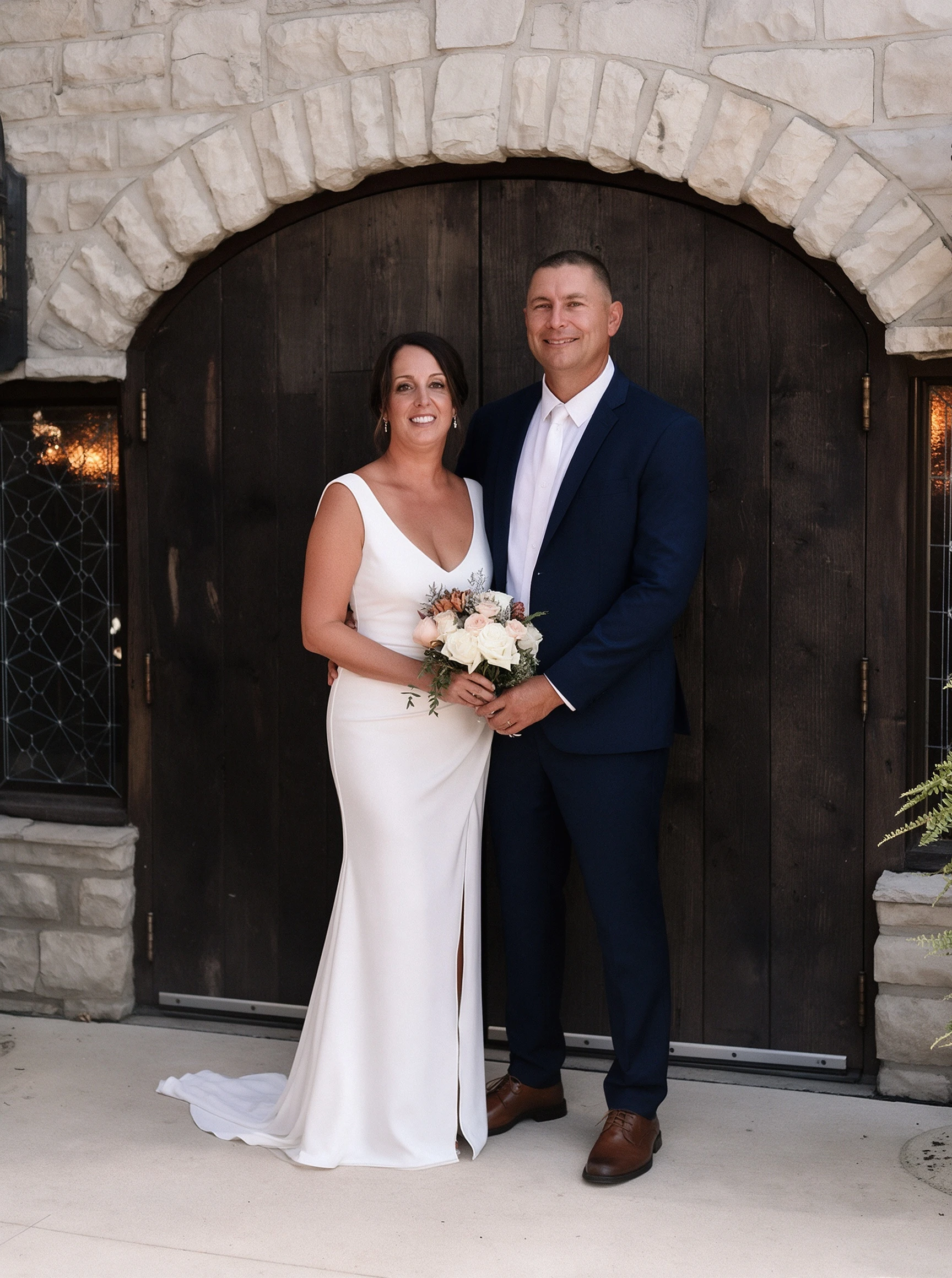 Bride and husband posing at winery doors in white crepe sheath wedding gown