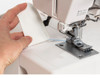 A close-up action shot of a hand pulling a completed piece of white fabric away from the machine, showing the chain stitch trailing off. Great for illustrating the chaining-off process and ease of finishing seams.