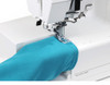 The machine with the flat bed removed, demonstrating the free-arm configuration. A teal knit tube (like a sleeve or legging) is being fed through the open arm area. "CoverPro 3000 Professional" branding and the FINE/STD switch are visible. Great for showcasing the free-arm capability.