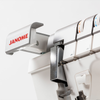 An extreme close-up of the Janome logo on the machine's upper arm, with the retractable Hi-Light sewing light visible just below. The color-coded tension dials and thread guides are softly blurred in the background. Good for highlighting the built-in lighting feature.