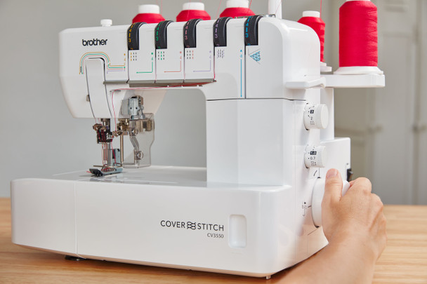 Hand adjusting control dials on Brother CV3550 cover stitch machine with color-coded threading guides visible