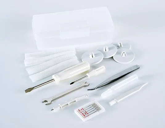 A flat-lay of the included accessories laid out against a clean white background. Visible items include the storage case, extra needles, tweezers, a screwdriver, a wrench, seam ripper, brush, and several spool caps and presser feet.