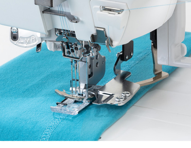 Top Cover Stitch in Action: A close-up action shot showing the machine actively stitching a top cover stitch on teal knit fabric. The needle plate, presser foot, and the built-in top cover hem guide are clearly visible, along with the L, M, R needle markings. Ideal for showcasing the signature top cover stitch feature.