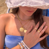 wearing gold shell necklace on gold filled chain layered with statement heart necklace at the beach wearing triangl bikini