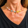 Close-up of a beaded necklace worn as a choker, with gold beads, a teal star, a neon yellow-green bead, a smiley face bead, and pink and lavender stones.