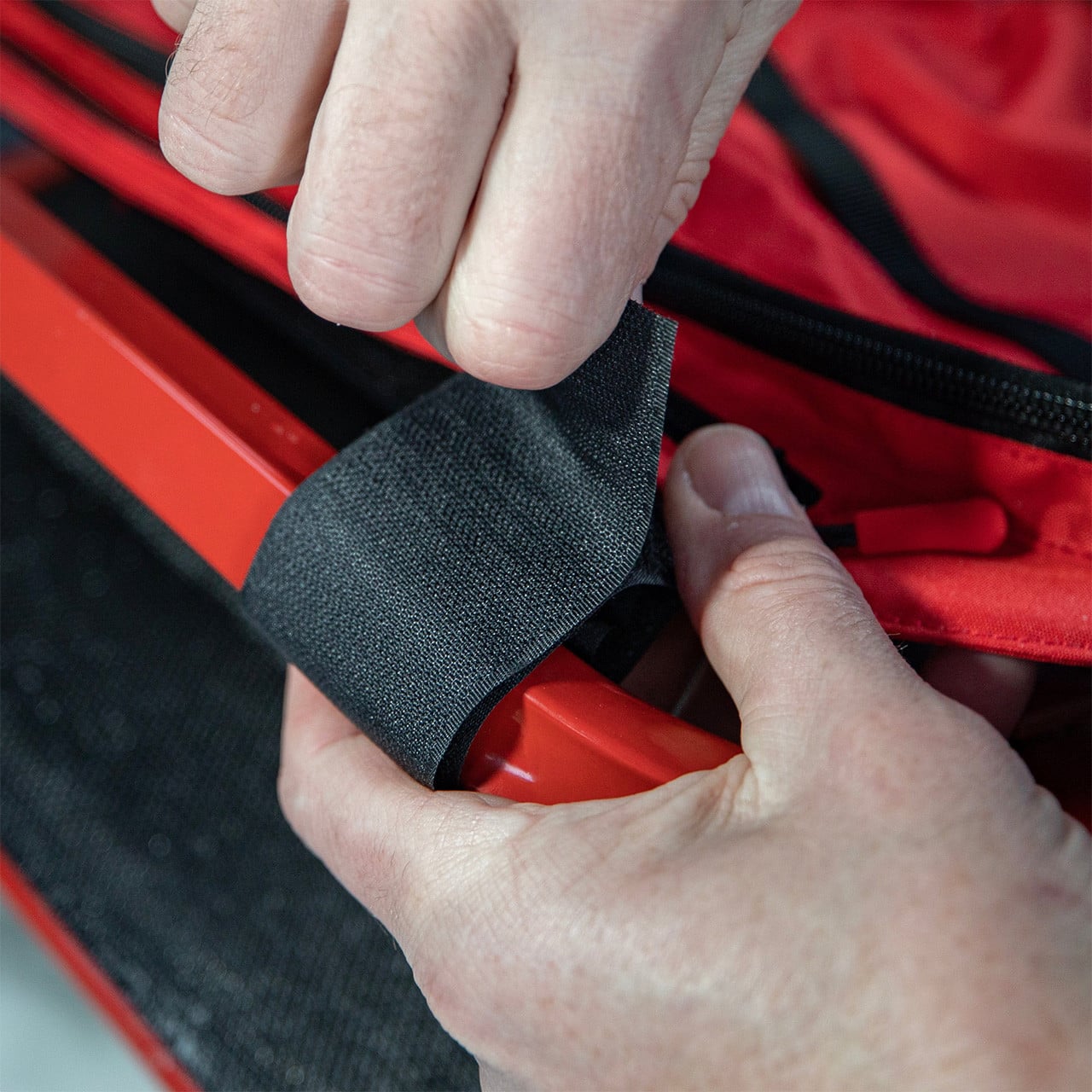 Close up of two hands strapping the hook and latch straps to frame of a shelter seat sold separately