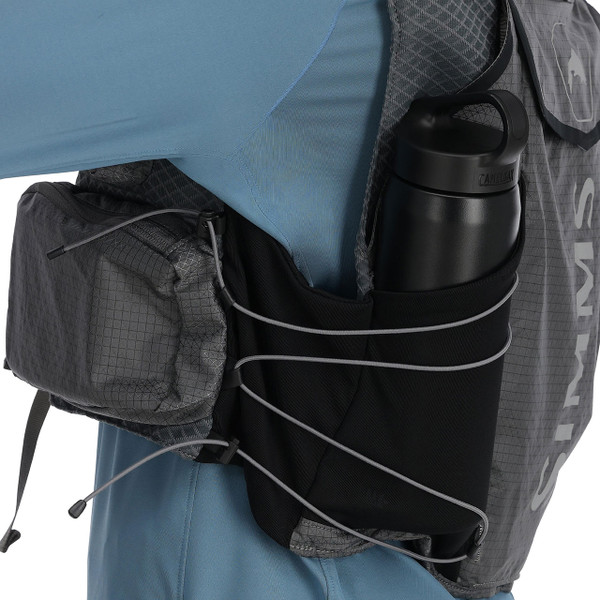 Simms Flyweight Vest on model side displaying compression bungee around mesh pocket holding water bottle, bottle not included