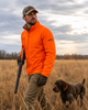 Man in blaze orange Wildfowler jacket and cap walks with a dog in a field.