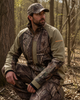 Man in Wildfowler Nature Brown camouflage soft shell jacket and pants, crouching in woods.