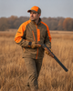 Man in tan and orange Wildfowler soft shell jacket holding a shotgun in a field.