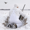 Wildfowler white snow waterproof bibs worn by a hunter kneeling in a snow-covered field with a shotgun.