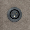Black round electrical outlet with two slots and a ground hole on a textured gray surface.