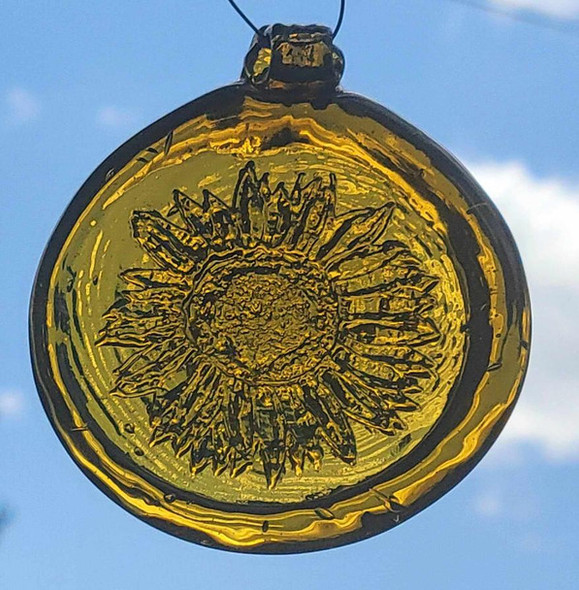 a yellow, round glass suncatcher with a relief image of a sunflower blossom