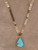 Genuine turquoise teardrop pendant on a polished gold arrow-link chain displayed on tan suede background.