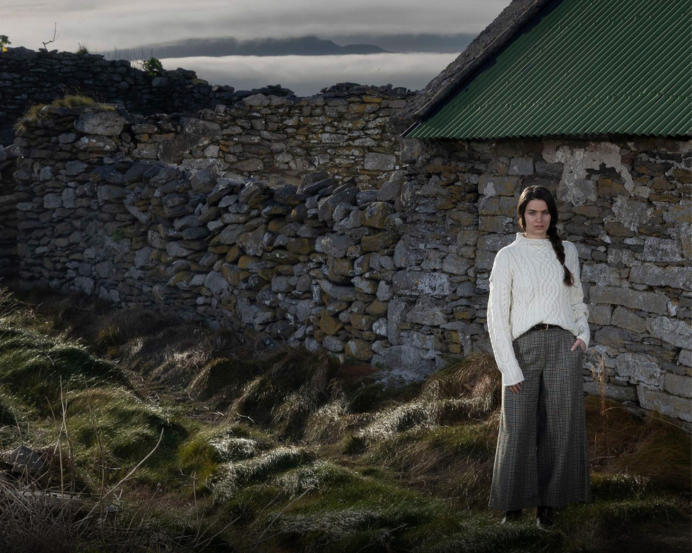 Woman in a cream Aran sweater beside a traditional island cottage