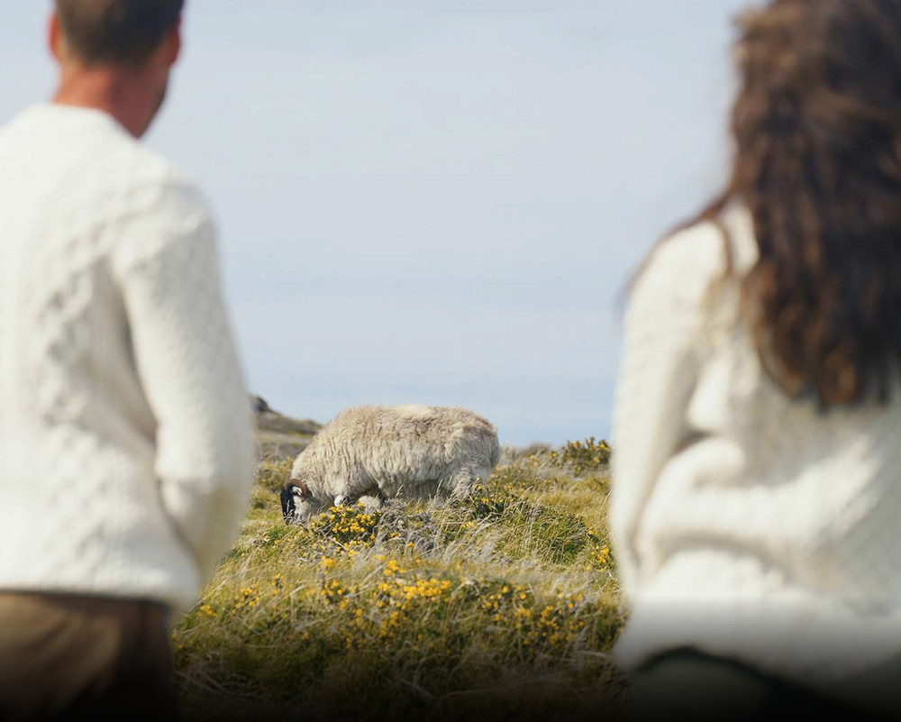 Two people in cream Aran sweaters walking through an island field