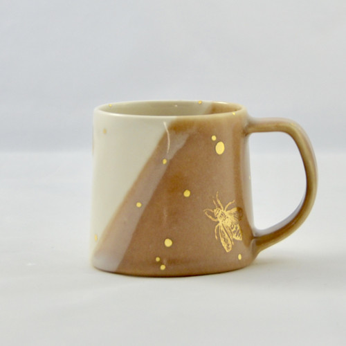 Start your morning off right with this hand thrown porcelain mug featuring three gold bees as well as äóìdropsäó of 22k gold luster. This two toned honey beige and white glazed mug holds around 10 to 12 oz, making it the perfect mug for your morning jolt of energy.