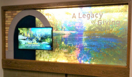 Display is built into an existing trophy wall case onsite. Campus slough photograph is imprinted on glass and backlit. Design includes a dimensional arch, lettering and a digital, touchscreen display.