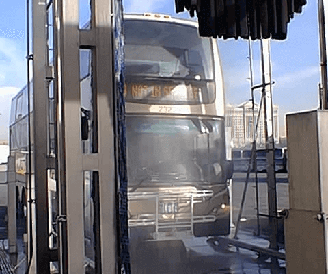 Extra large bus driving through an outdoor car wash system.