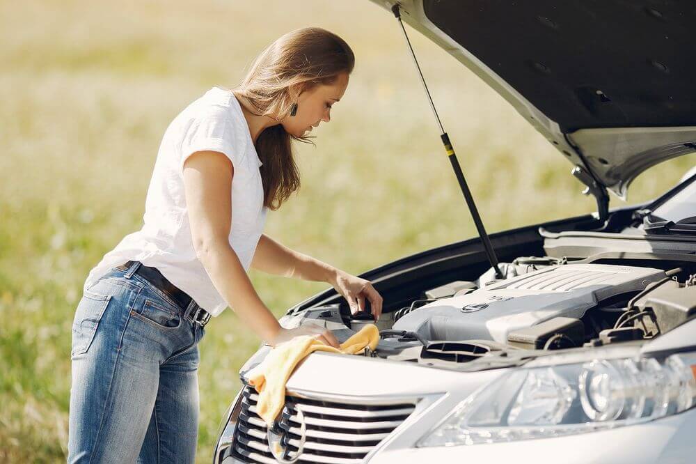 a woman looking under the hood of her car