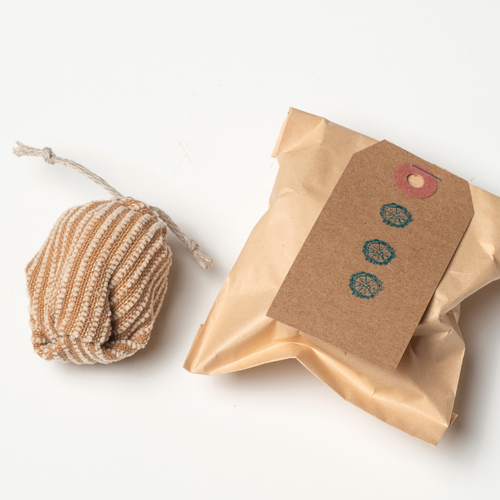 Image shows a small brown striped cat toy tied on one end with hemp twine. The toy is the size of a chicken egg. It sits on a white background next to a small brown paper bag. The tag on the bag is dark brown with 3 small blue stamped images.
