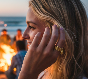 A close-up shot of a model's hand wearing the Uno de 50 Lock Ring on her index finger, showcasing its bold design. Set on a firebom beach background.