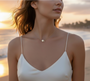 A model with dark hair wearing the gold Midnight Sun pearl and moissanite necklace, which sits elegantly on her collarbone with a white top.