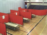 Red rolling partition panels creating enclosed areas with tables and chairs inside a gymnasium.