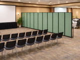 Large green wheeled partition dividing a conference or event room with rows of chairs.