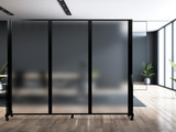 Frosted wheeled divider panels separating areas in a modern office with wood floors and large windows.