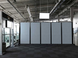 Large open interior with a long row of gray wheeled divider panels blocking part of a terminal-like space.