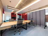 Modern meeting room with long wooden tables and rolling gray partition panels creating a semi-private workspace.