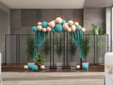 Balloon arch with teal and cream draping set in front of gray rolling partition panels, flanked by potted plants in a modern indoor space.