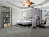 Bedroom with a gray rolling partition separating a workspace desk from the bed in a bright home interior.