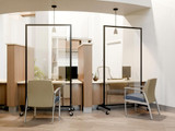 Reception desks separated by clear wheeled divider panels, with chairs in a bright office setting.